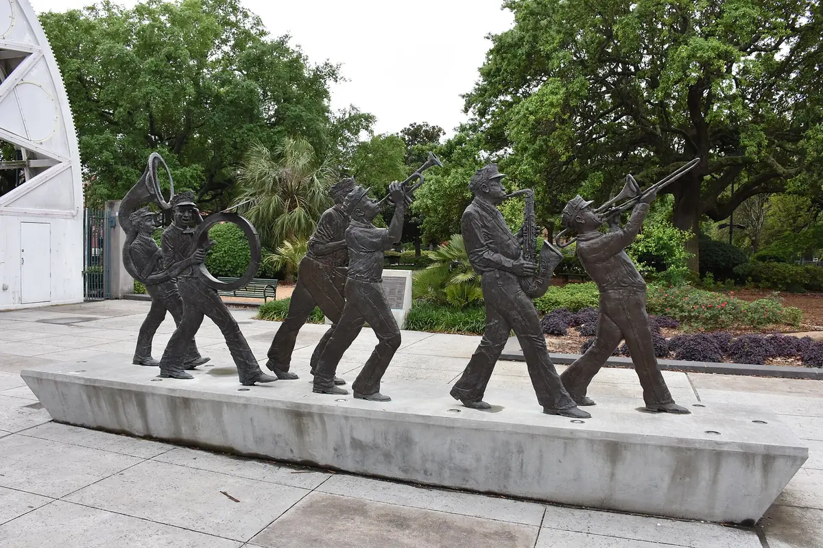 Bronze statues of a brass band in step, with trumpets, a saxophone and a sousaphone, on a low concrete plinth in Louis Armstrong Park